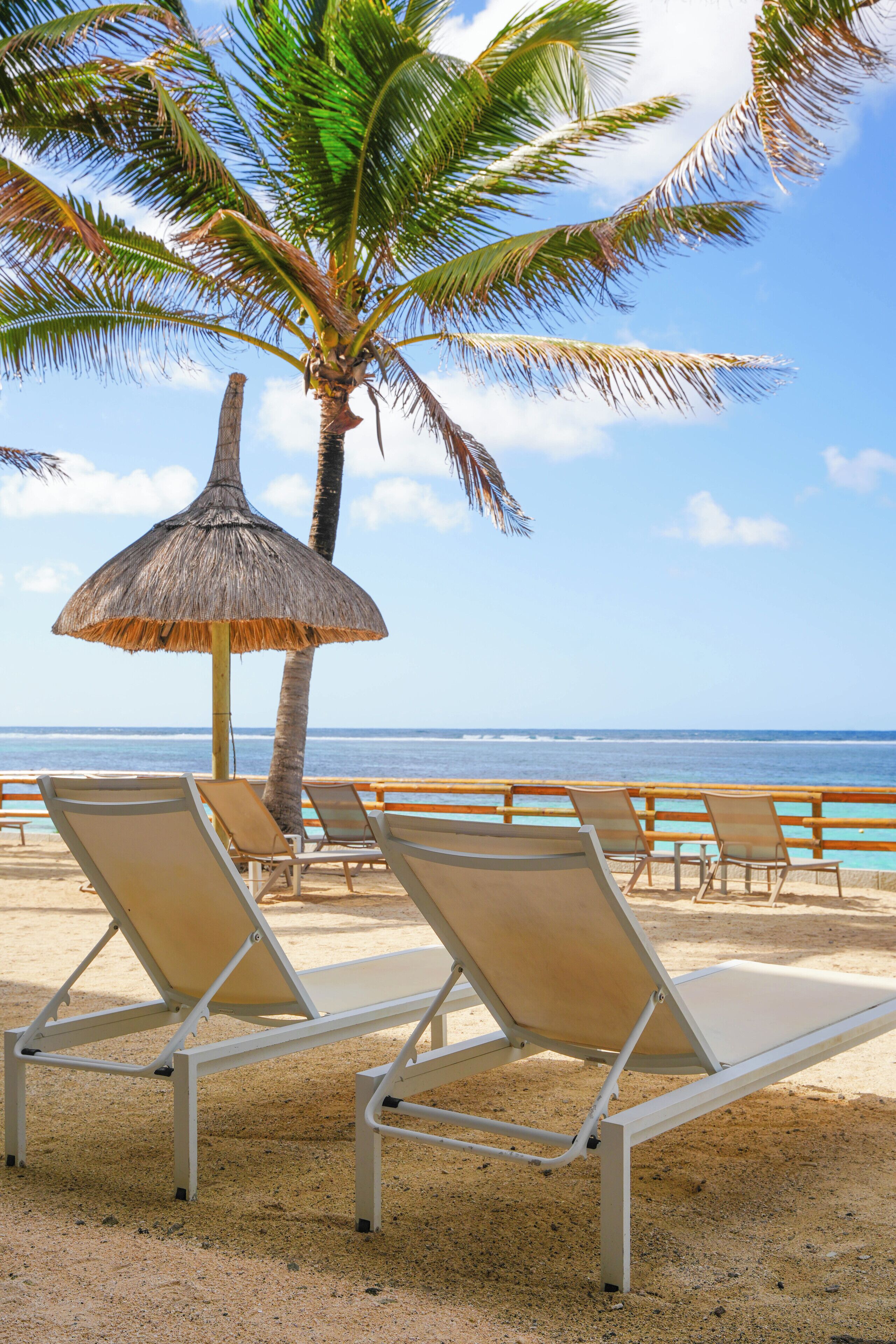 A beach with lounge chairs and a thatched umbrella.