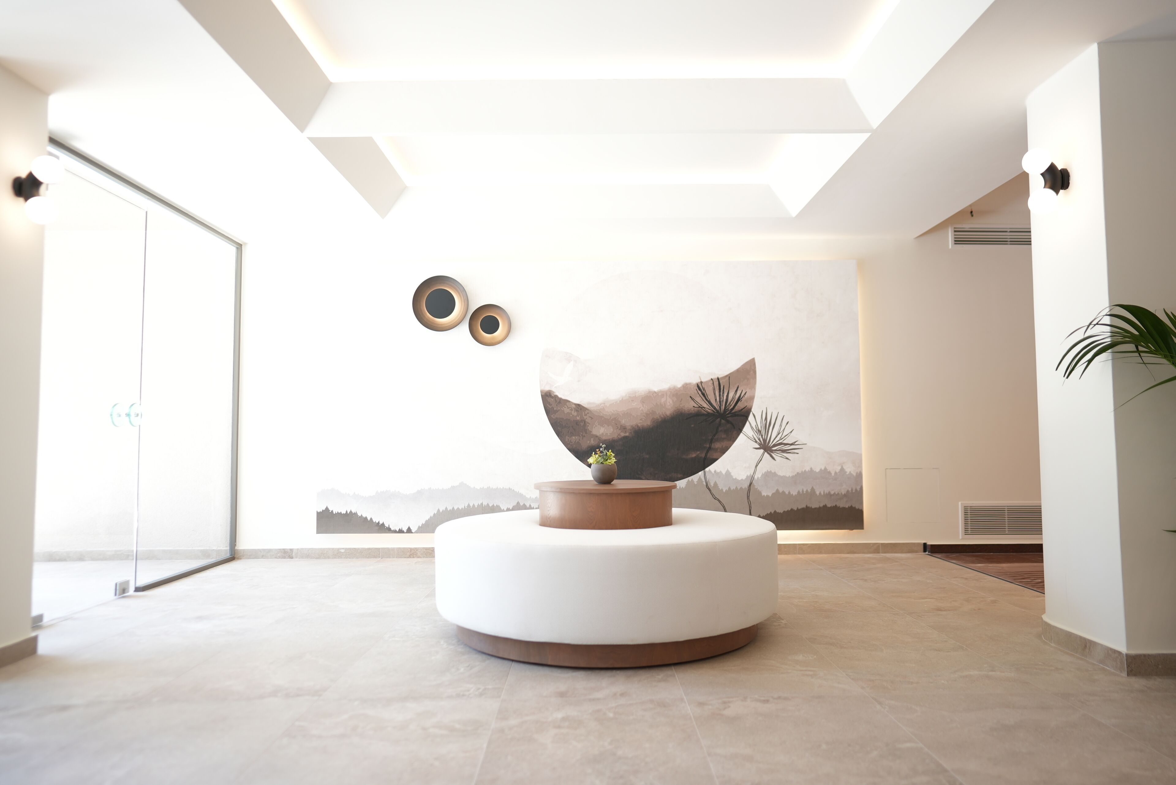 A modern lobby with a circular seating area, a large wall mural, and a glass door entrance.