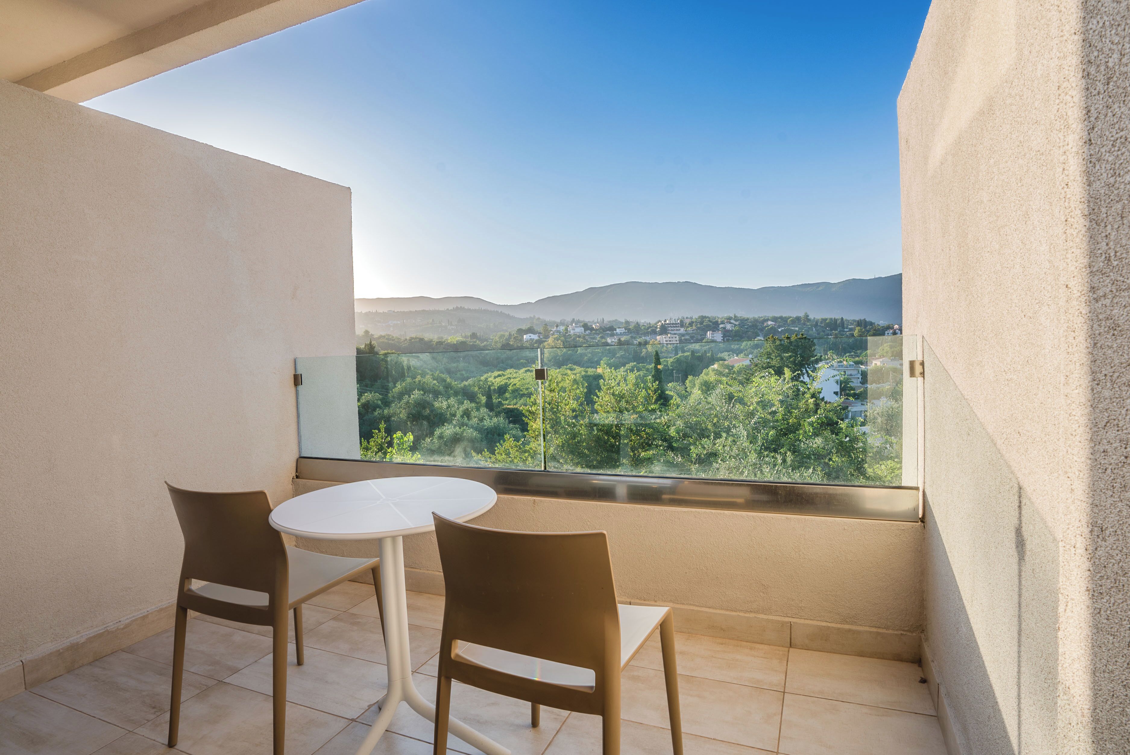 A balcony with a white table and two chairs, overlooking a scenic view of hills and greenery.