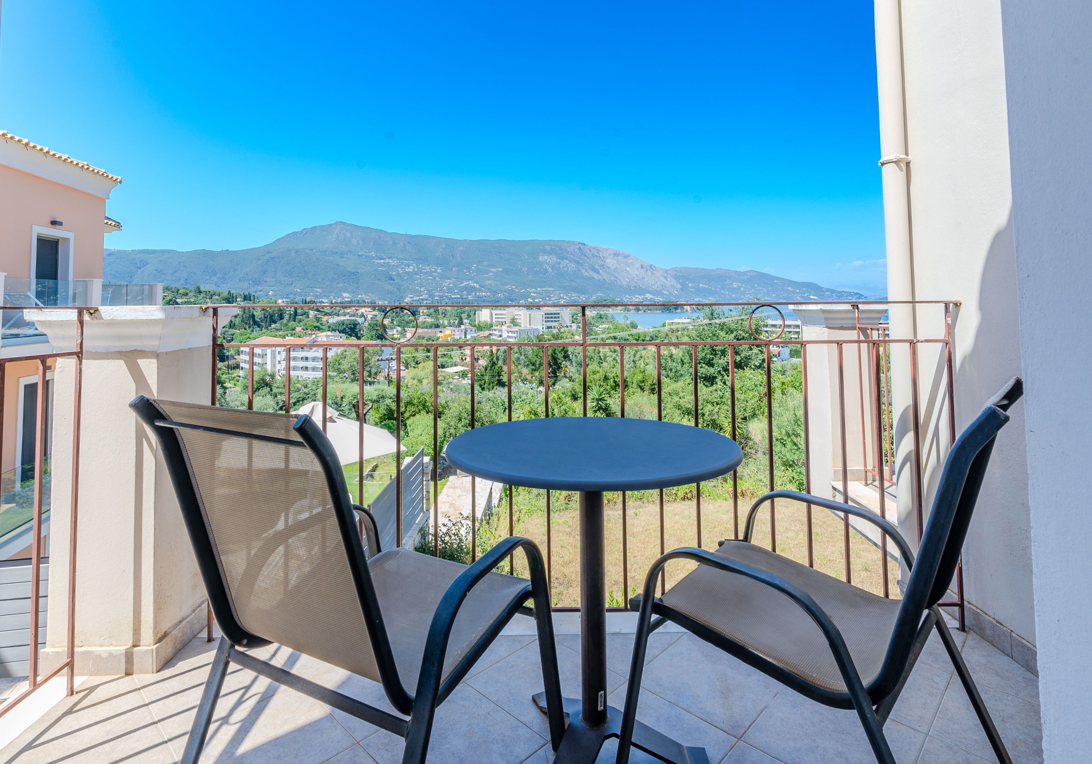 Un balcón con dos sillas y una mesa pequeña, con vistas a un paisaje urbano y montañas.