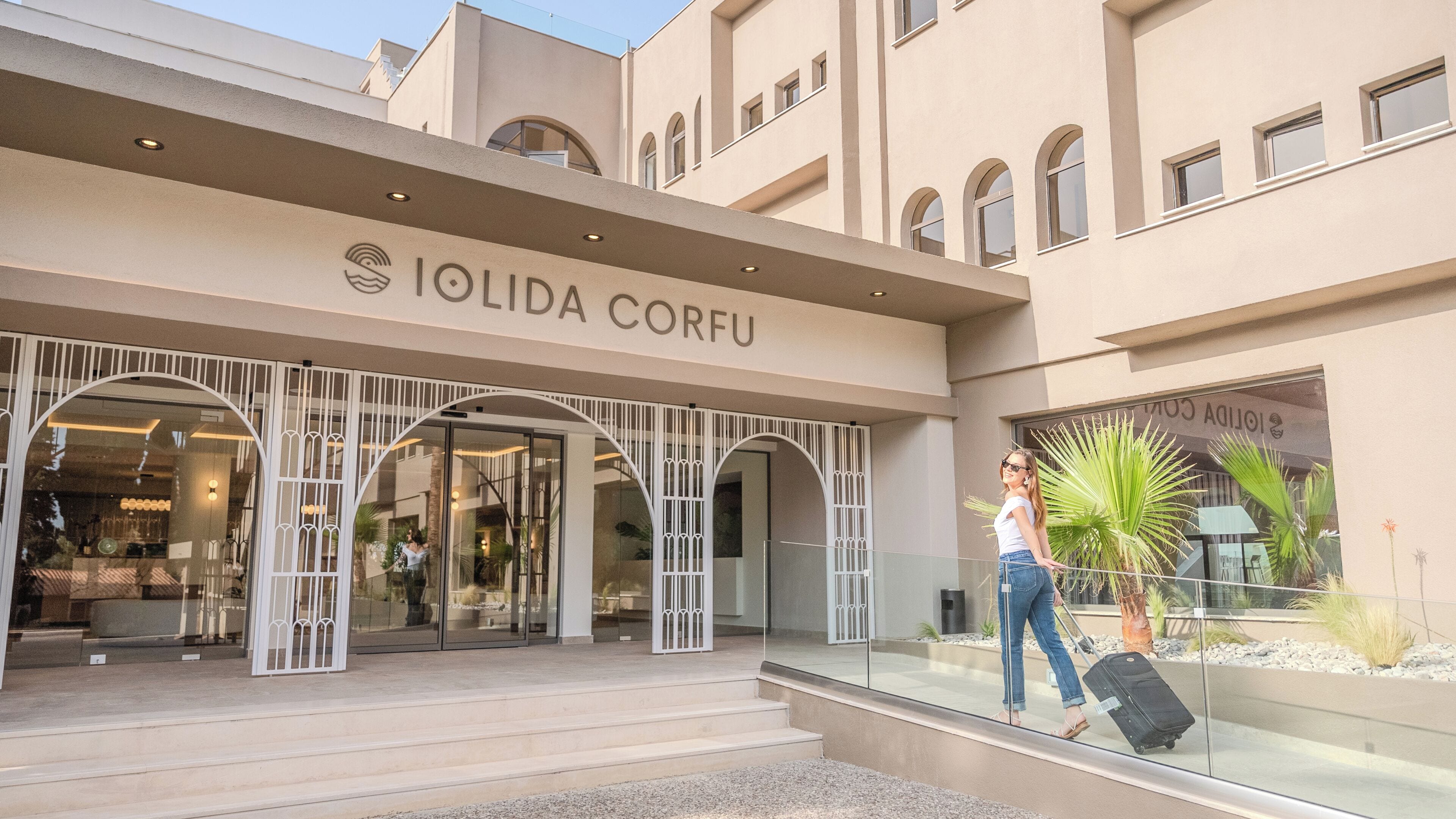 The exterior of the Iolida Corfu hotel with a modern design, featuring arched entrances and a clear view of the interior through the glass doors.