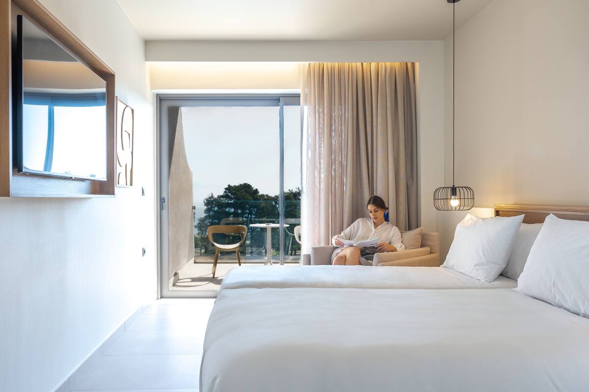 A modern hotel room with a large bed, a balcony with a view, and a small table with chairs.