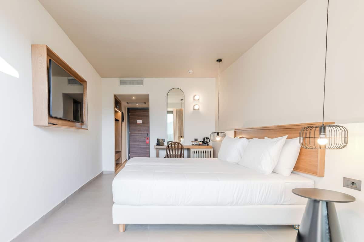 A modern hotel room with a large bed, a desk, a chair, and a mirror.