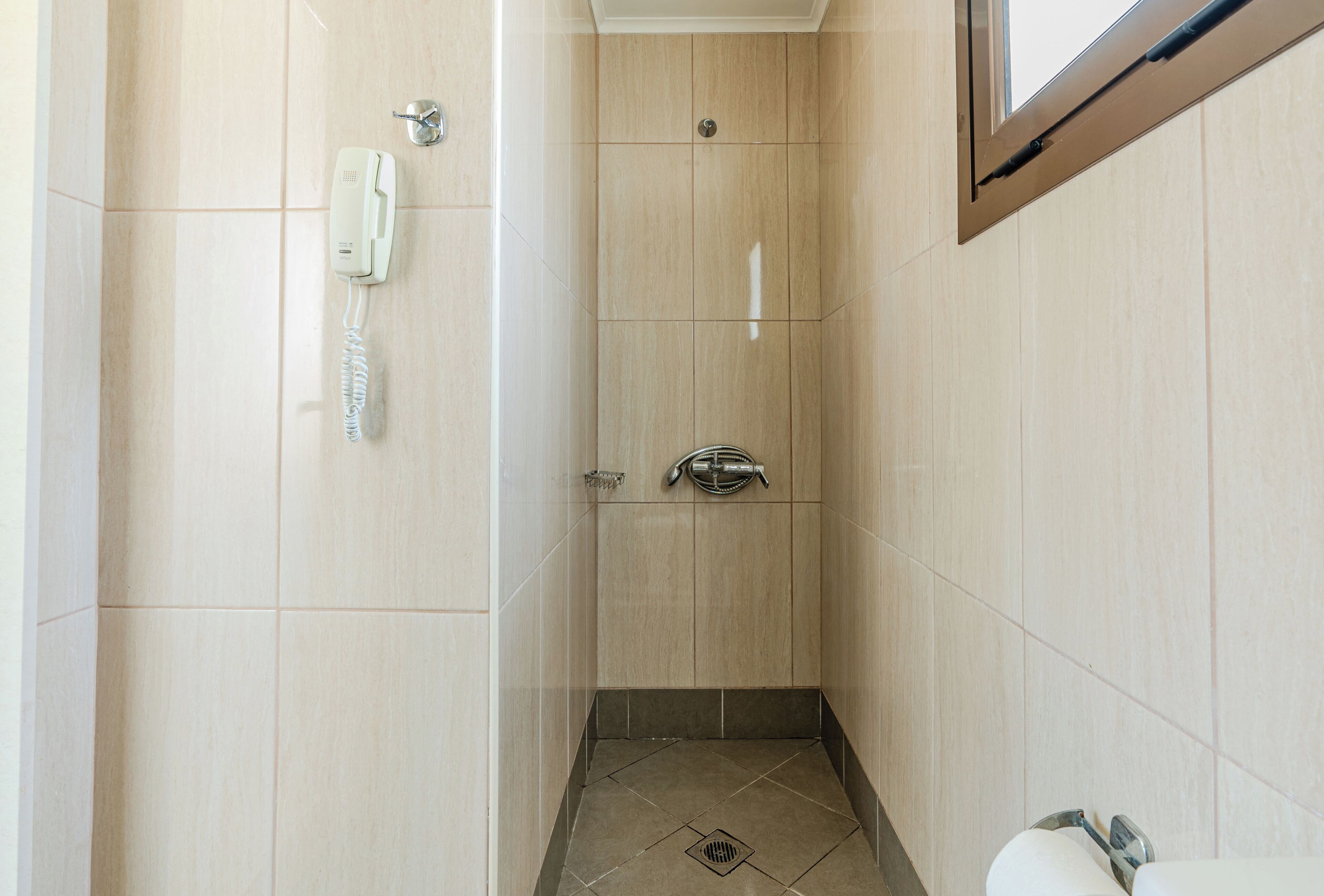 A small, narrow bathroom with a shower, a toilet, and a telephone.