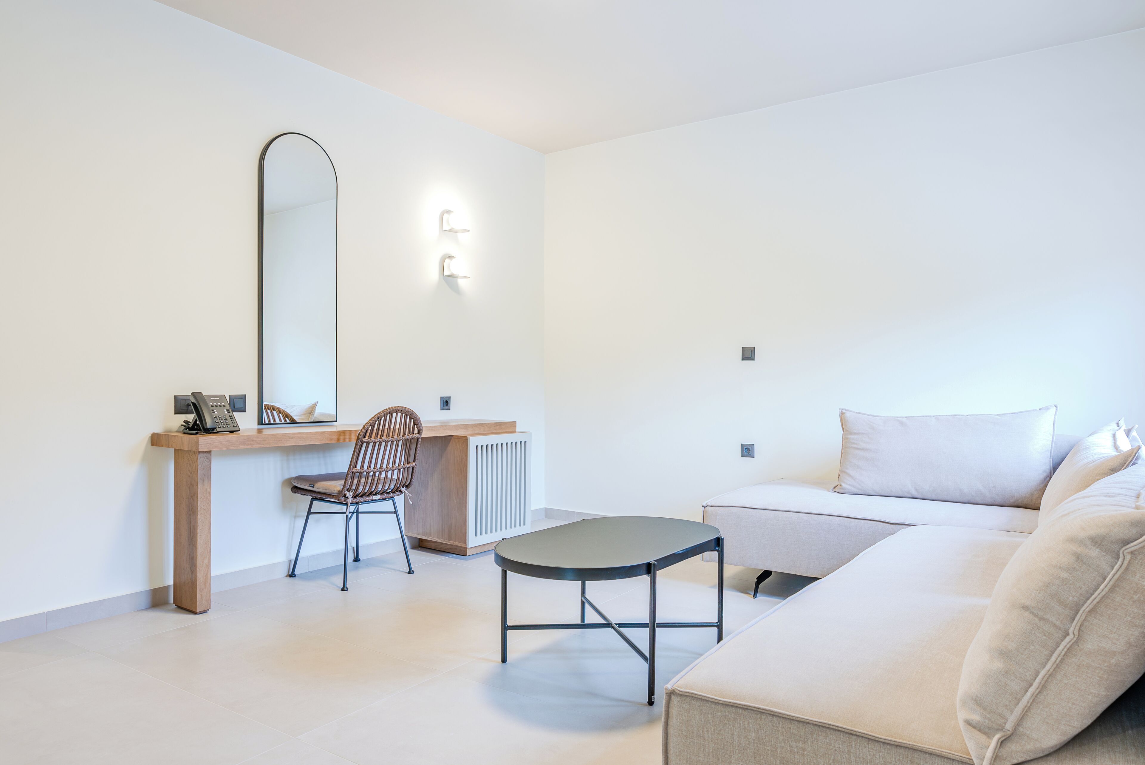 Een moderne, minimalistische woonkamer met een bank, een tafeltje, een stoel, een bureau en een grote spiegel.
