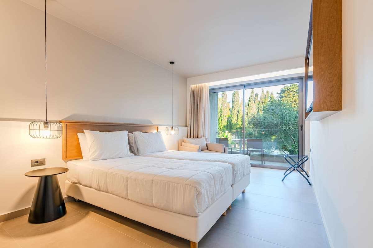 A modern bedroom with a large bed, bedside tables, and a view of greenery through a window.