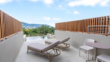 Une terrasse sur le toit, équipée de deux chaises longues, d’une table et offrant une vue sur une piscine et un paysage lointain.