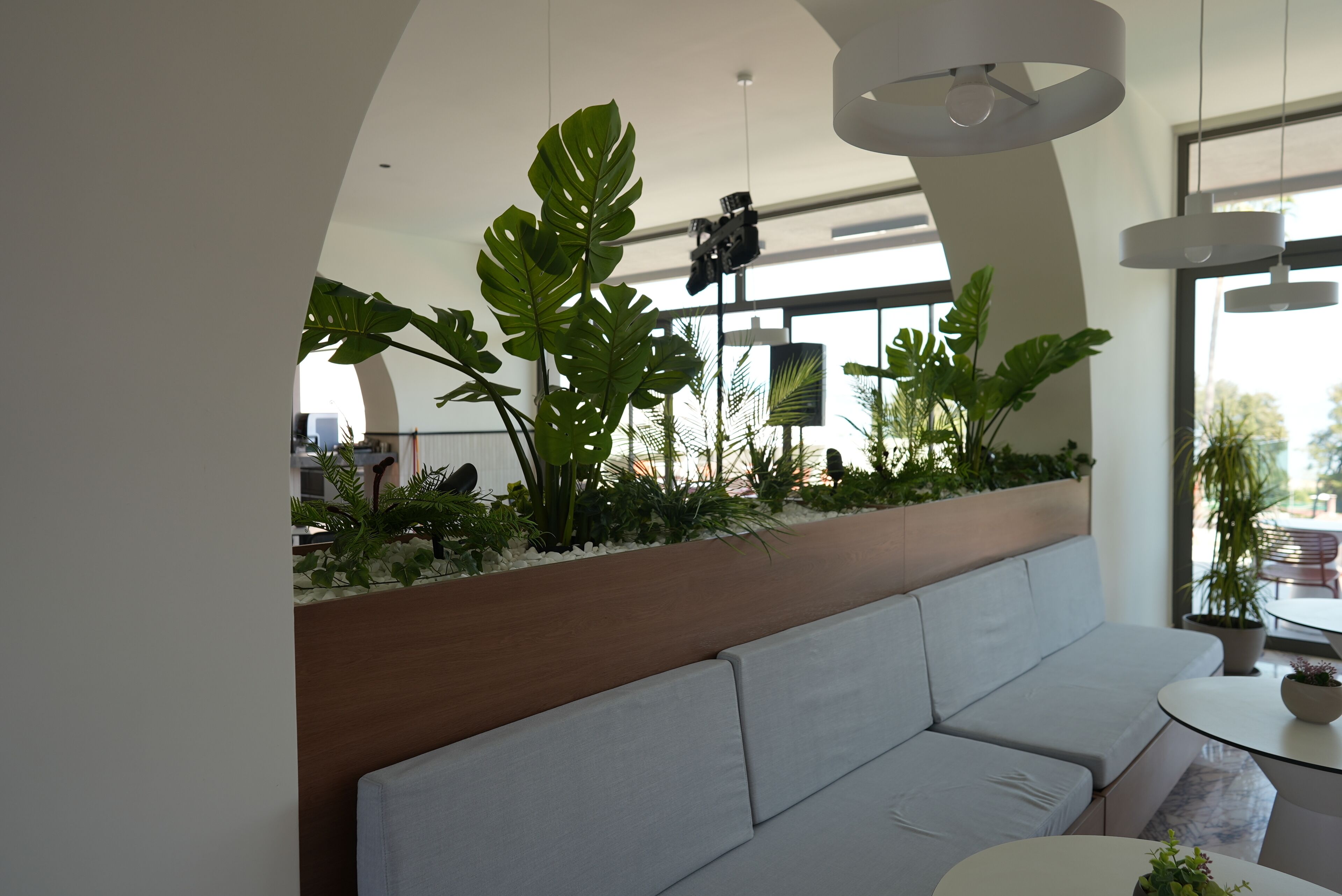 Un intérieur moderne avec un canapé blanc, un pot de fleurs en bois contenant des plantes tropicales et un appareil photo suspendu.