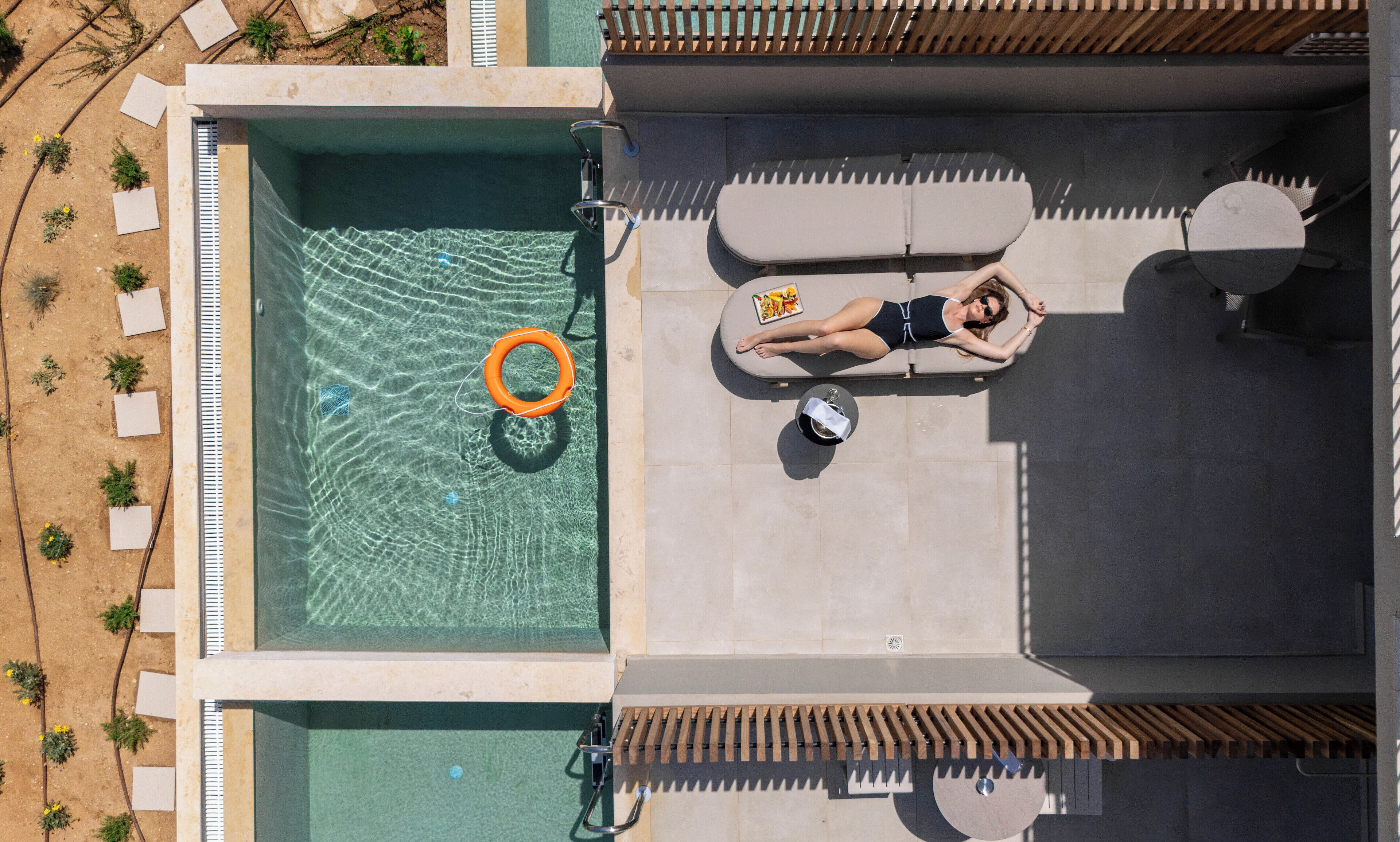 An aerial view of a swimming pool with a lounge area, including a sunbed and a poolside table.