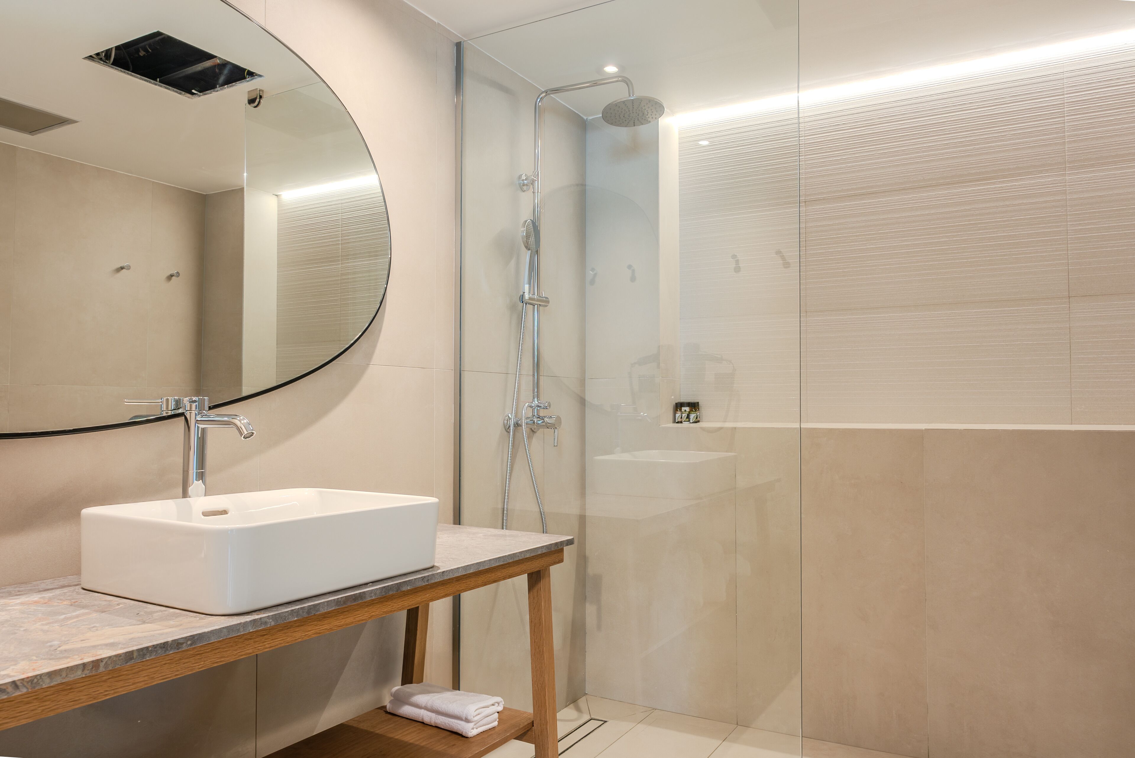 Een moderne badkamer met een witte wastafel, een houten opbergmeubel, een glazen douchecabine en een grote spiegel.
