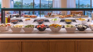Un bufé con diversos platos presentados en recipientes, con un ventanal grande que da a una vista panorámica de la ciudad.