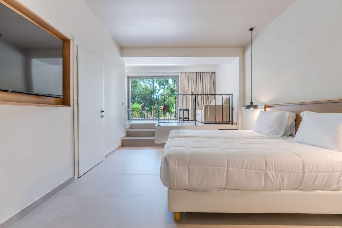 A modern bedroom with a large bed, a TV mounted on a wall, and a view of the outdoors through a sliding door.