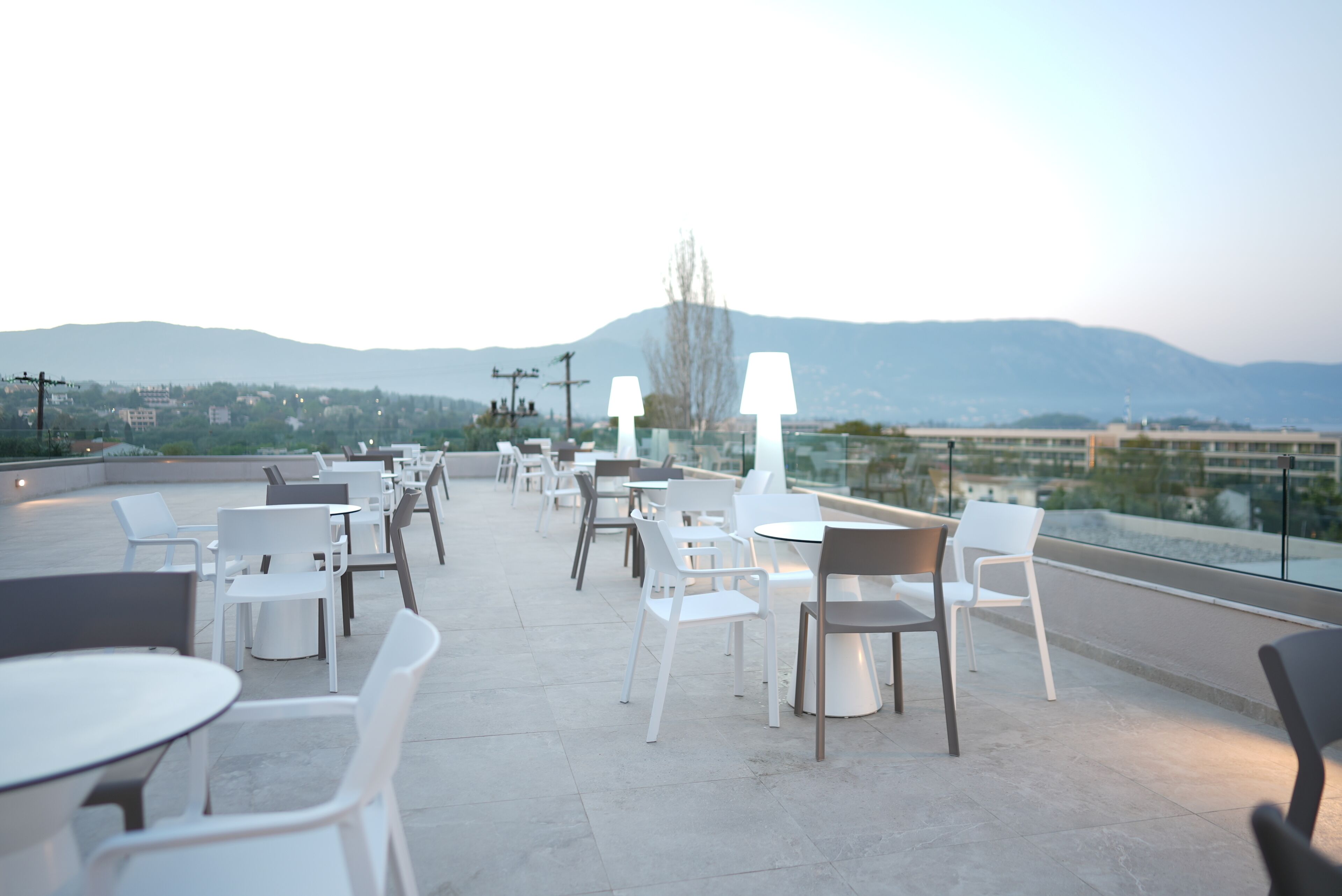 Un área de estar al aire libre con mesas y sillas, con vistas a un paisaje urbano y montañas.