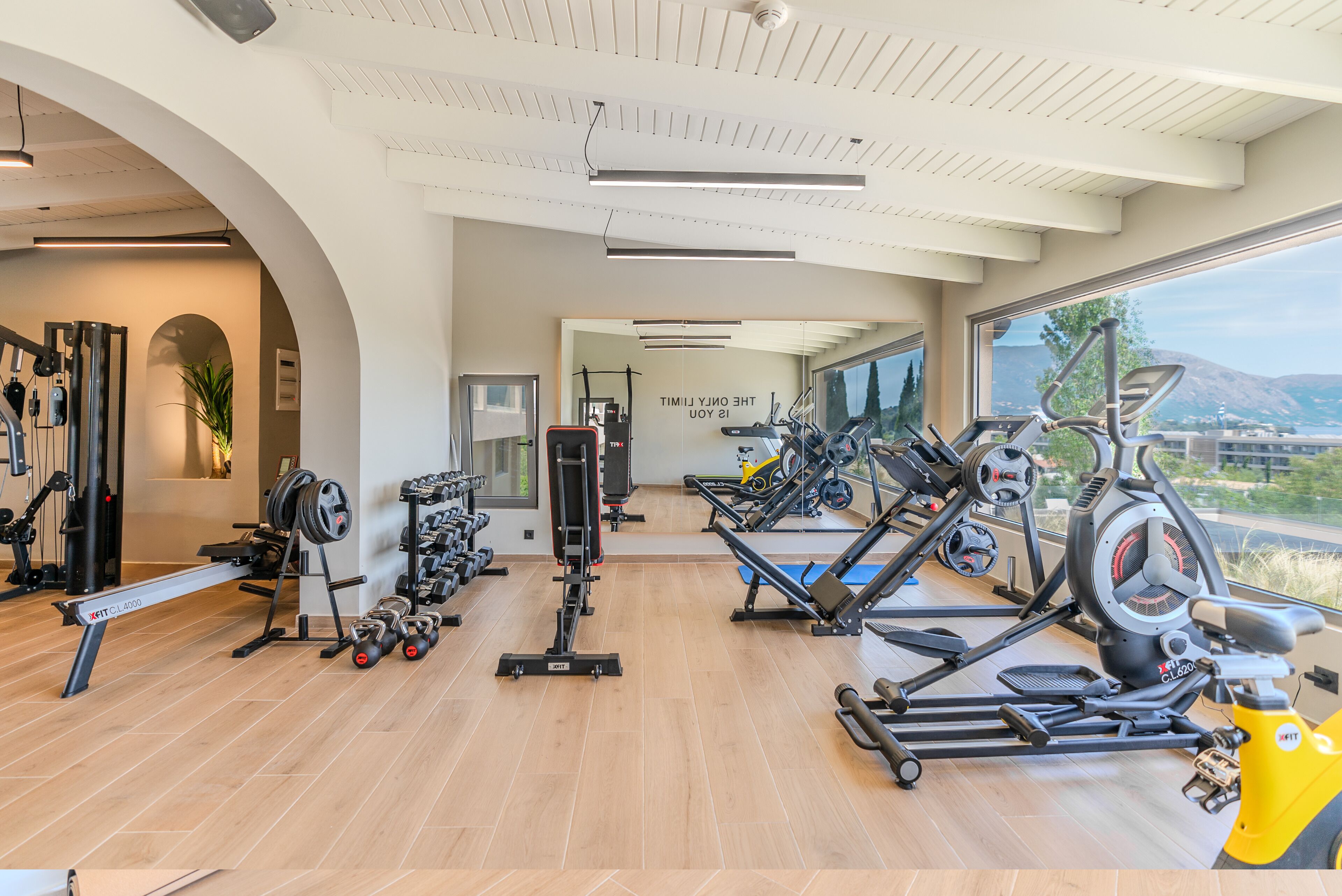 Een moderne sportschool met diverse fitnessapparaten, een rek voor gewichten en een groot raam met uitzicht op de omgeving.