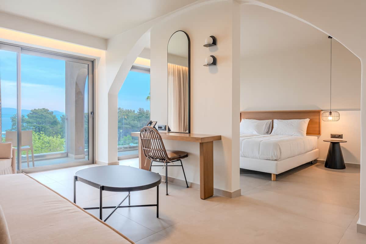 A modern bedroom with a bed, a desk, and a chair. There is a large window providing a view of the outdoors.
