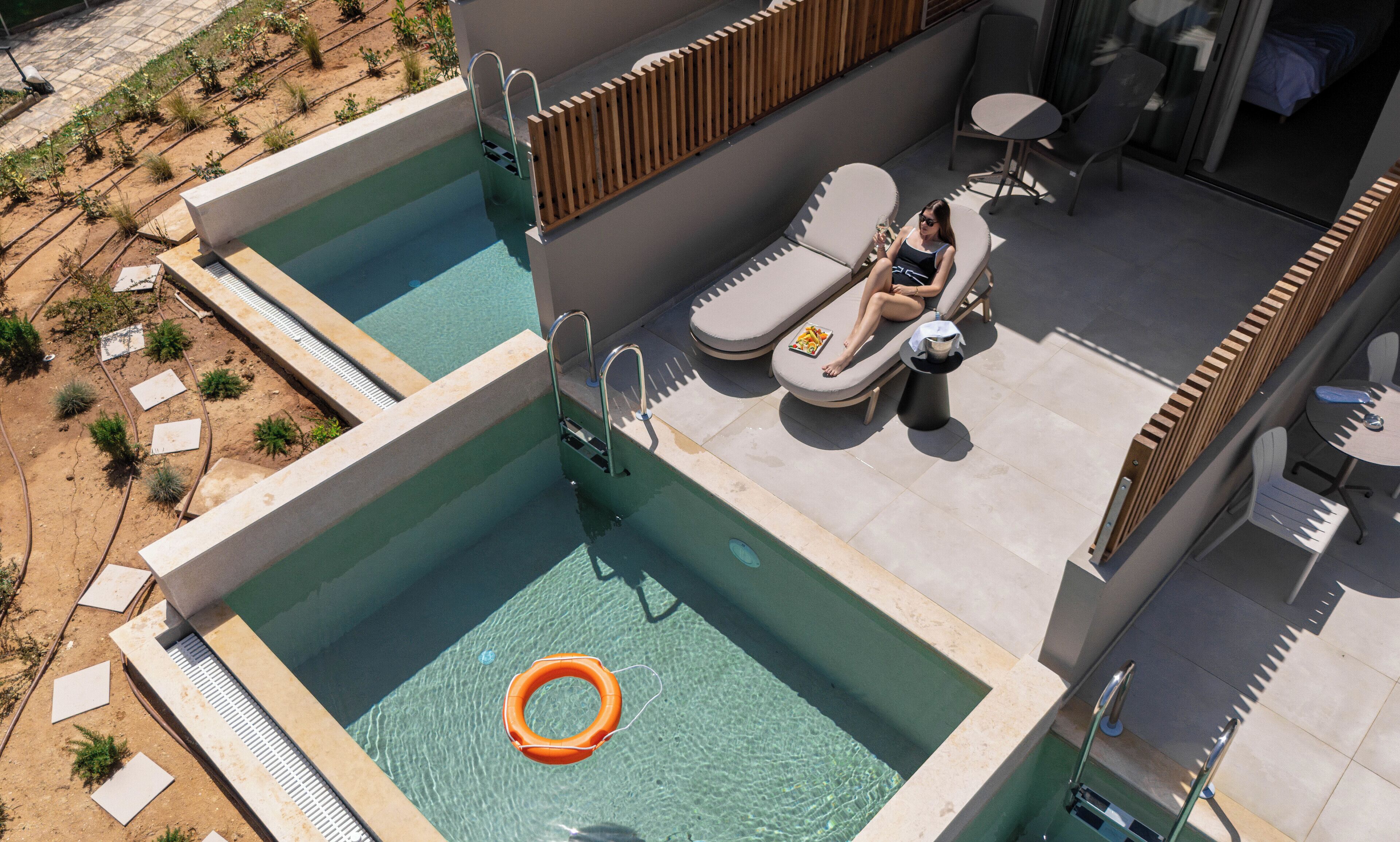 A rooftop pool area with two separate pools, lounge chairs, and a small table.