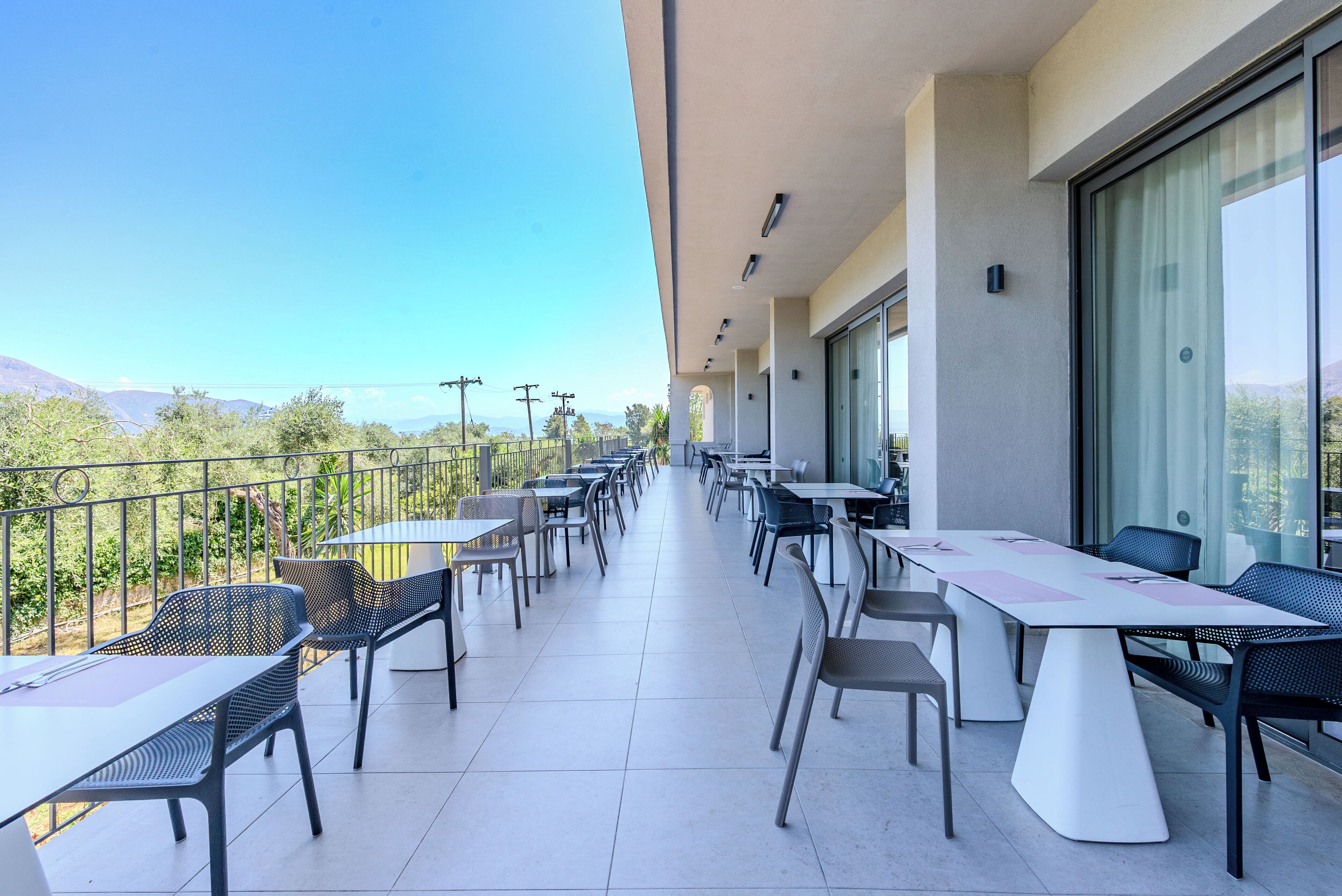 A balcony with tables and chairs, offering a view of the landscape.