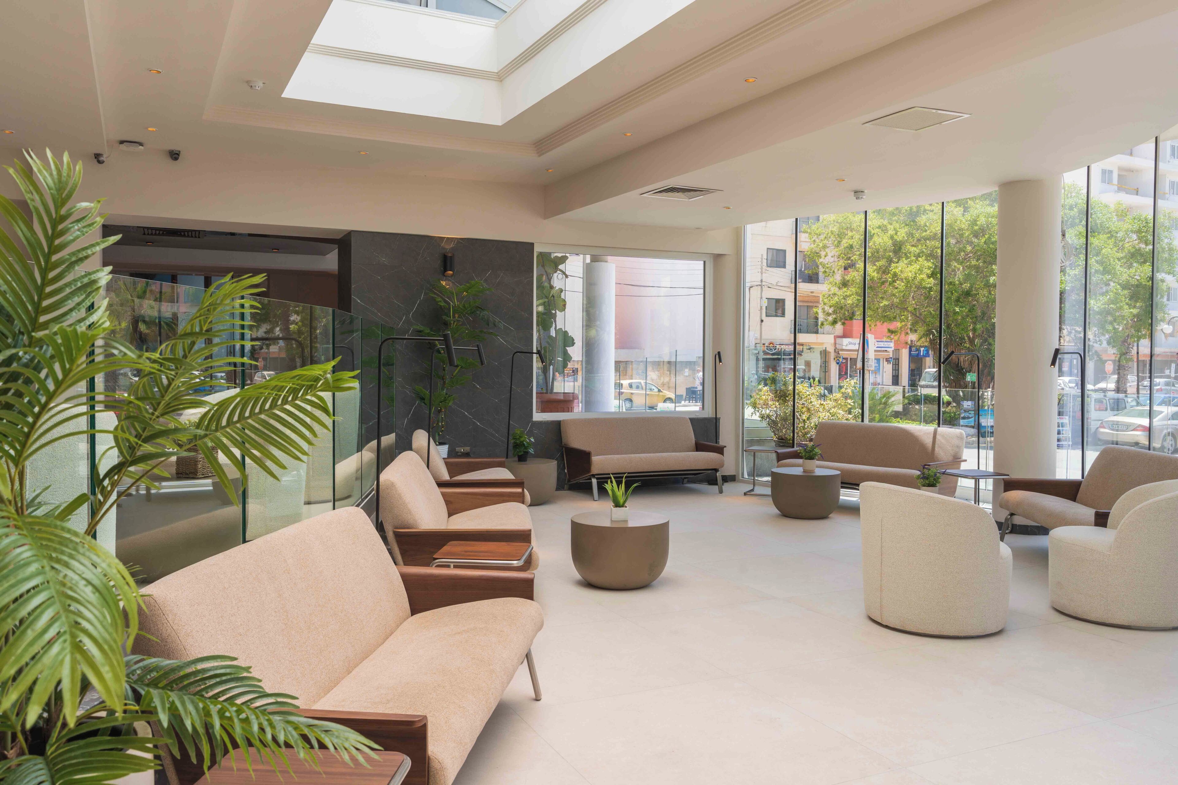 Eine moderne Lobby mit Sitzbereichen, großen Fenstern und Zimmerpflanzen.