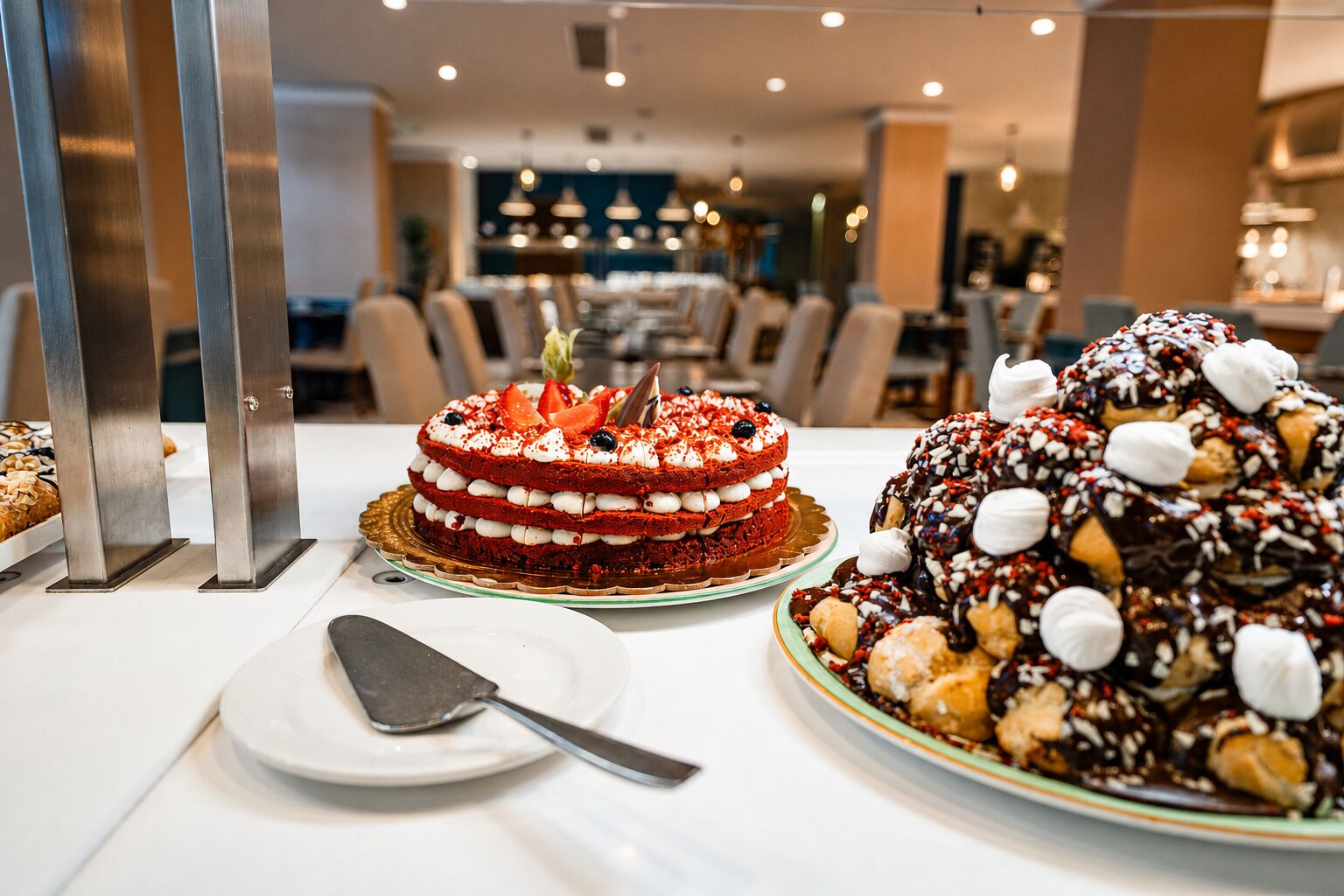Una presentación de postres con un pastel de terciopelo rojo en capas, un pastel con cobertura de chocolate y un plato con una espátula para pasteles.