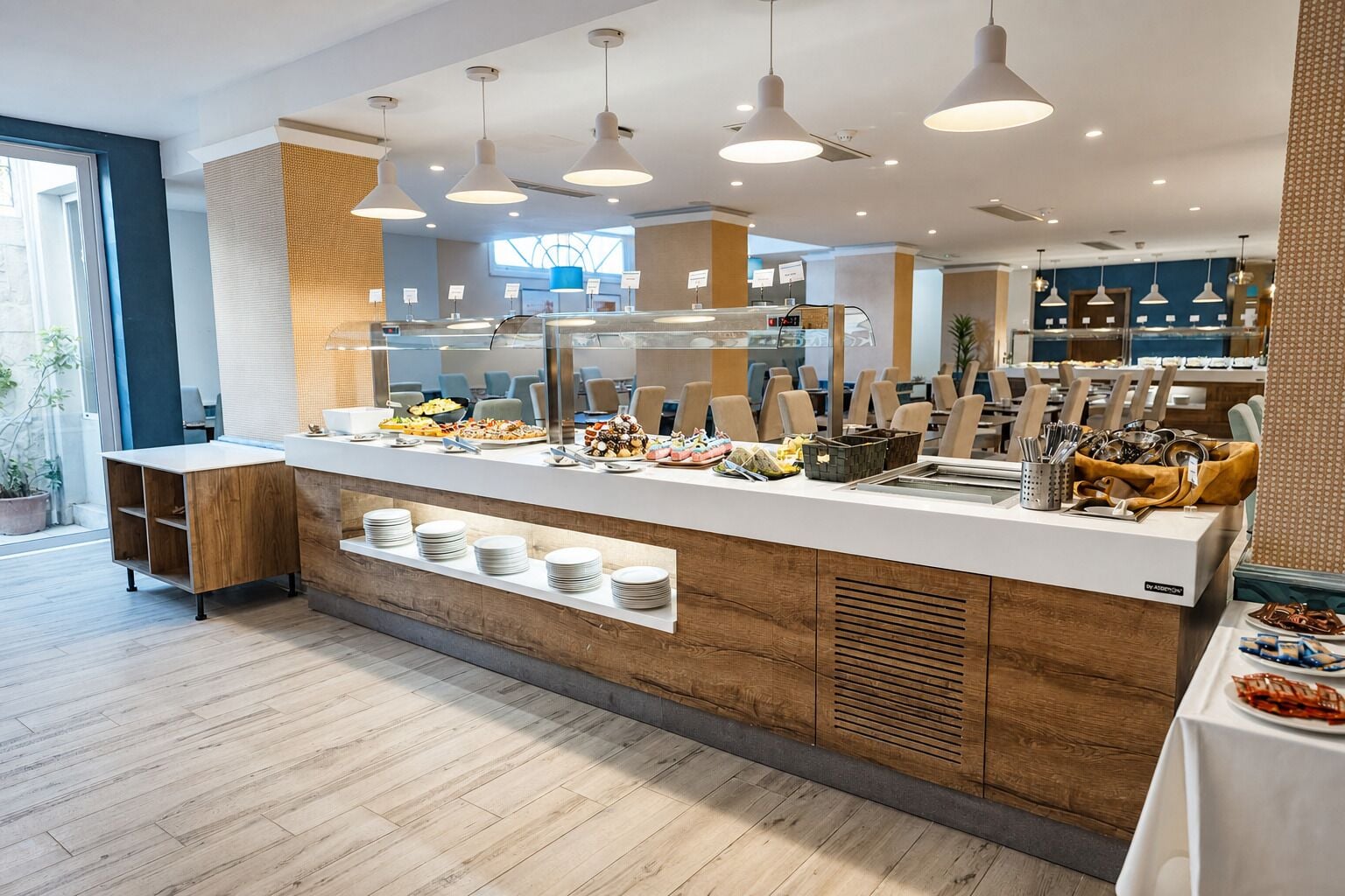 A modern buffet setup with a variety of food items, a counter with plates, and a seating area with chairs.