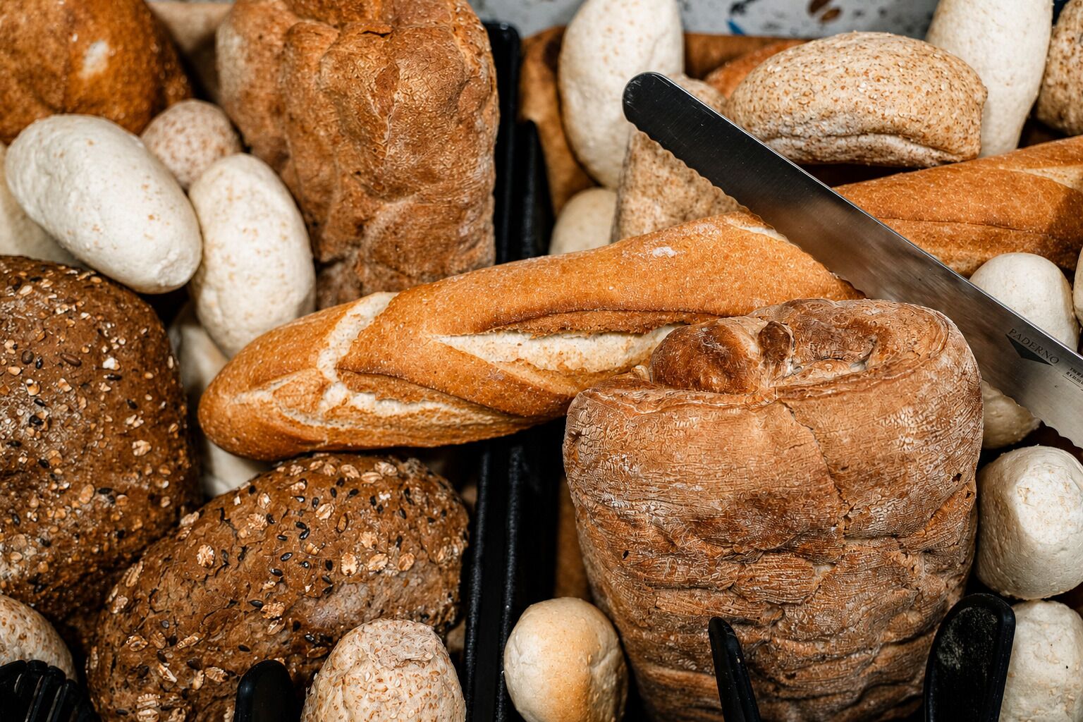 A variety of breads and rolls, including a baguette and a round loaf, displayed in a basket.