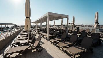 A sunlit outdoor seating area with rows of lounge chairs and umbrellas, overlooking a body of water.