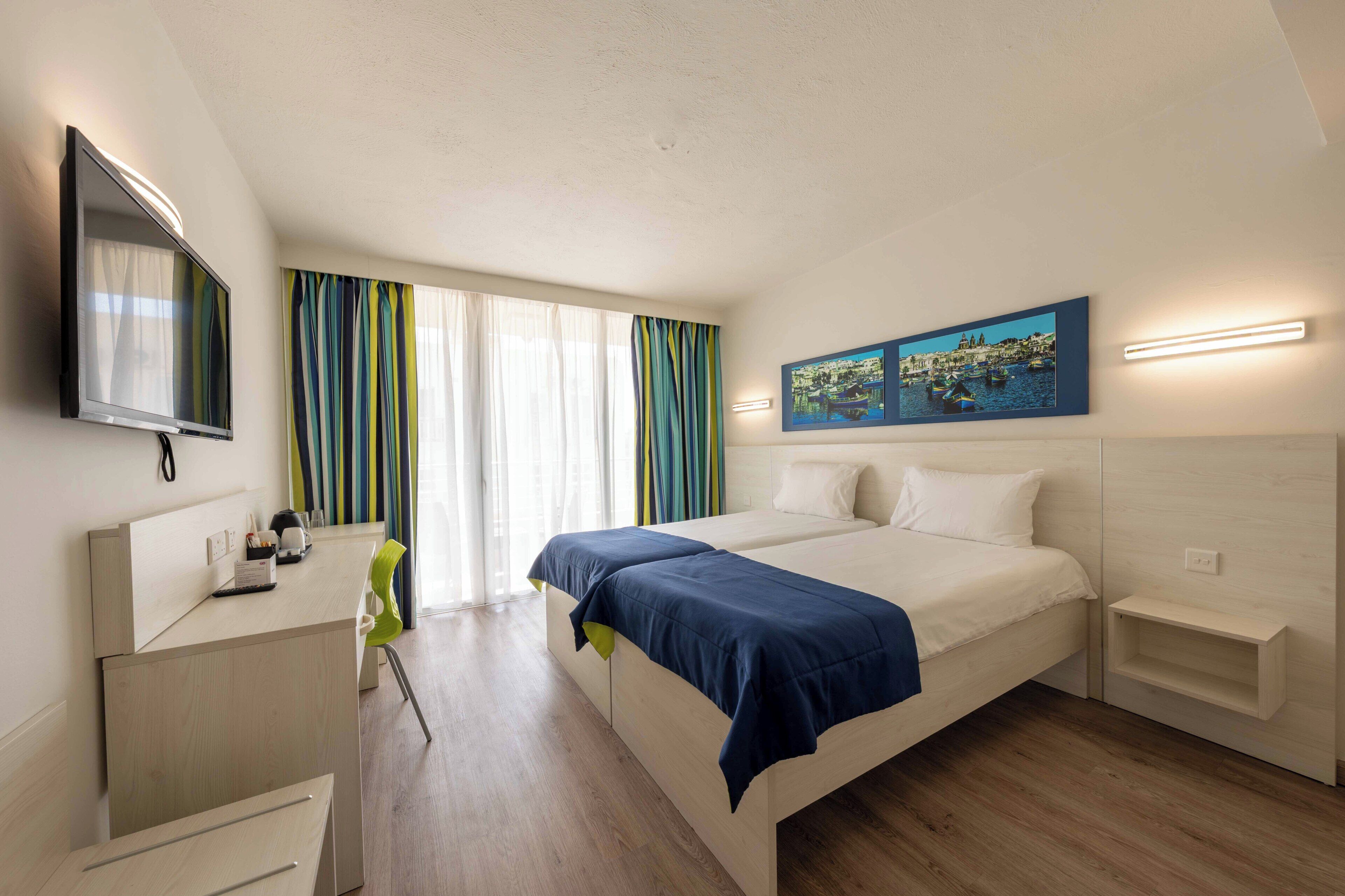 Habitación de hotel con cama, escritorio, silla, televisión y un cuadro en la pared.