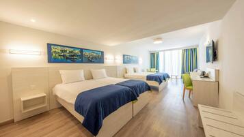 A hotel room with two beds, a desk, and a chair. There are paintings on the wall and a television mounted on the wall.