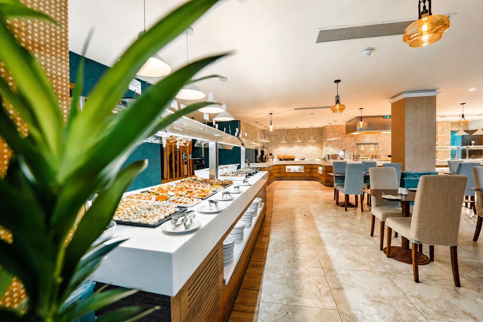 A buffet area with a variety of food items, a seating area with tables and chairs, and a modern interior design with pendant lighting.