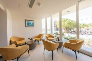 Un interior moderno con una zona de estar que incluye cuatro sillones y una mesa redonda, grandes ventanales con vistas a la calle y una obra de arte enmarcada en la pared.