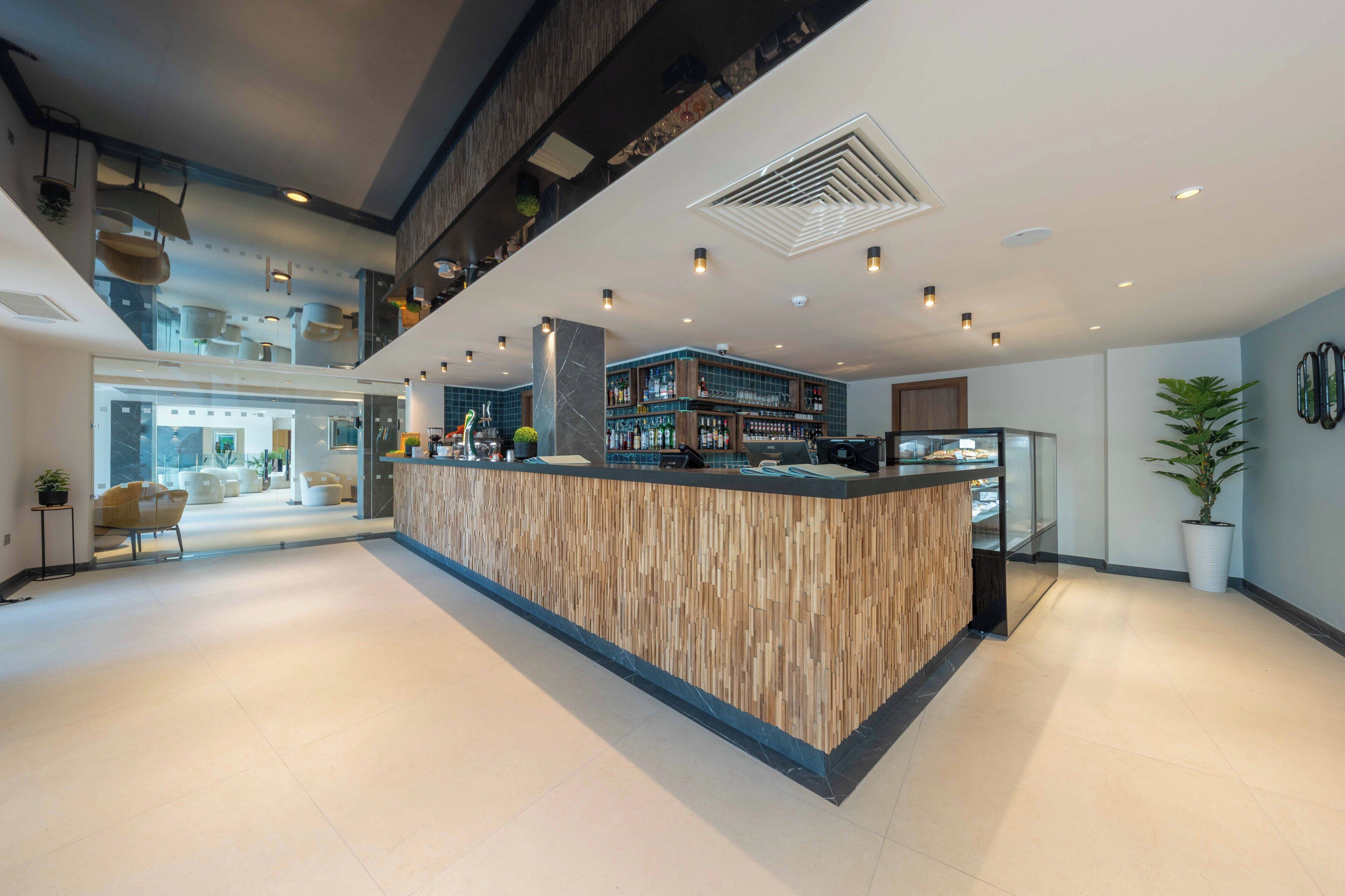 A modern bar area with a wooden counter, a mezzanine level, and a view of the lobby.