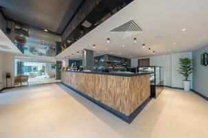 Zona bar moderna con un bancone in legno, un soppalco e vista sulla hall.