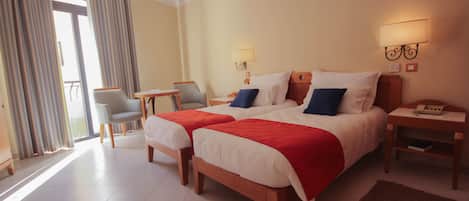 A hotel room with two beds, a chair, a table, and a nightstand.