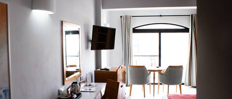 A hotel room with a bed, a desk with a chair, a television, and a large window with curtains.
