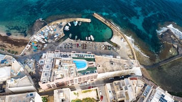 Vista aérea de una zona costera con un puerto deportivo, edificios y una piscina.
