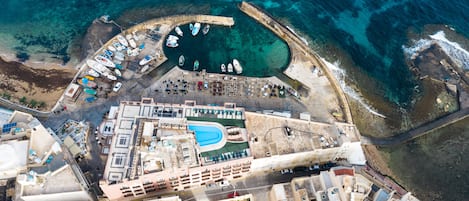 An aerial view of a coastal area with a marina, buildings, and a swimming pool.
