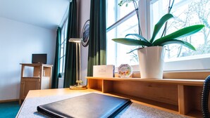 A neatly arranged desk with a laptop, a lamp, a potted plant, and a small shelf with decorative items. - Hoftaferne Neuburg (Neuburg am Inn)