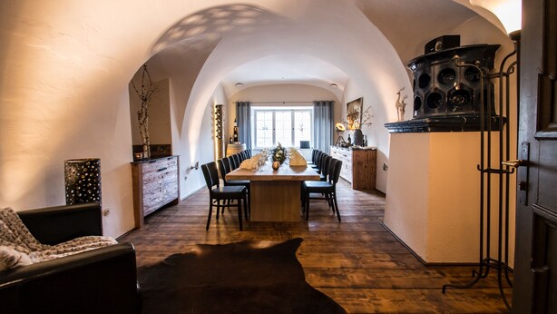 A cozy dining area with a wooden table and chairs, a sofa, and a fireplace. - Hoftaferne Neuburg (Neuburg am Inn)