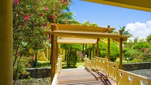 A wooden bridge with white railings leading to a covered area with a stone wall and lush greenery. - Silver Beach (Trou d'Eau Douce)