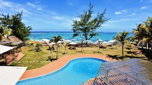 A resort pool with a view of the ocean, surrounded by palm trees and beach umbrellas. - Silver Beach (Trou d'Eau Douce)