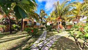 A tropical garden with palm trees, a stone pathway, and a building with a light-colored facade. - Silver Beach (Trou d'Eau Douce)