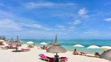 A beach with sun loungers and thatched umbrellas.