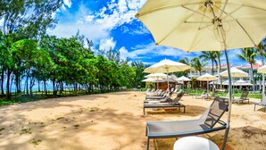 A beachside resort with sun loungers and umbrellas, a sandy beach, and a backdrop of palm trees and a building. - Tarisa Resort (Mont Choisy)