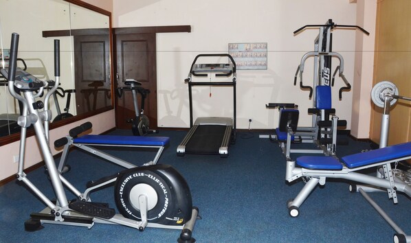 Une salle de sport équipée de divers appareils, notamment un tapis de course, un vélo elliptique et des appareils de musculation.