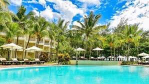 A swimming pool with lounge chairs and umbrellas, surrounded by palm trees and a building with balconies. - Tarisa Resort (Mont Choisy)
