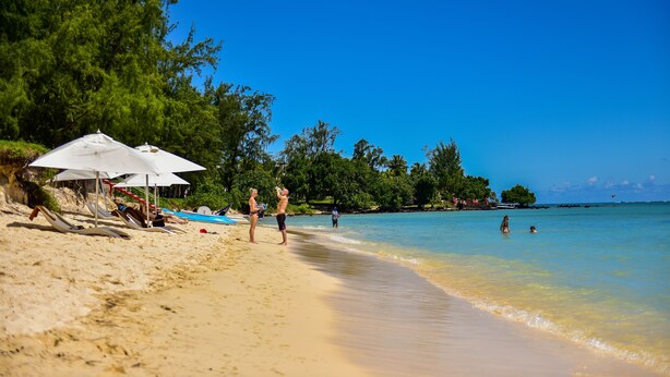 A beach with umbrellas, beach chairs, and people enjoying the water. - Tarisa Resort (Mont Choisy)