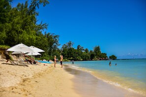 Une plage avec des parasols, des chaises longues et des gens qui profitent de la mer.