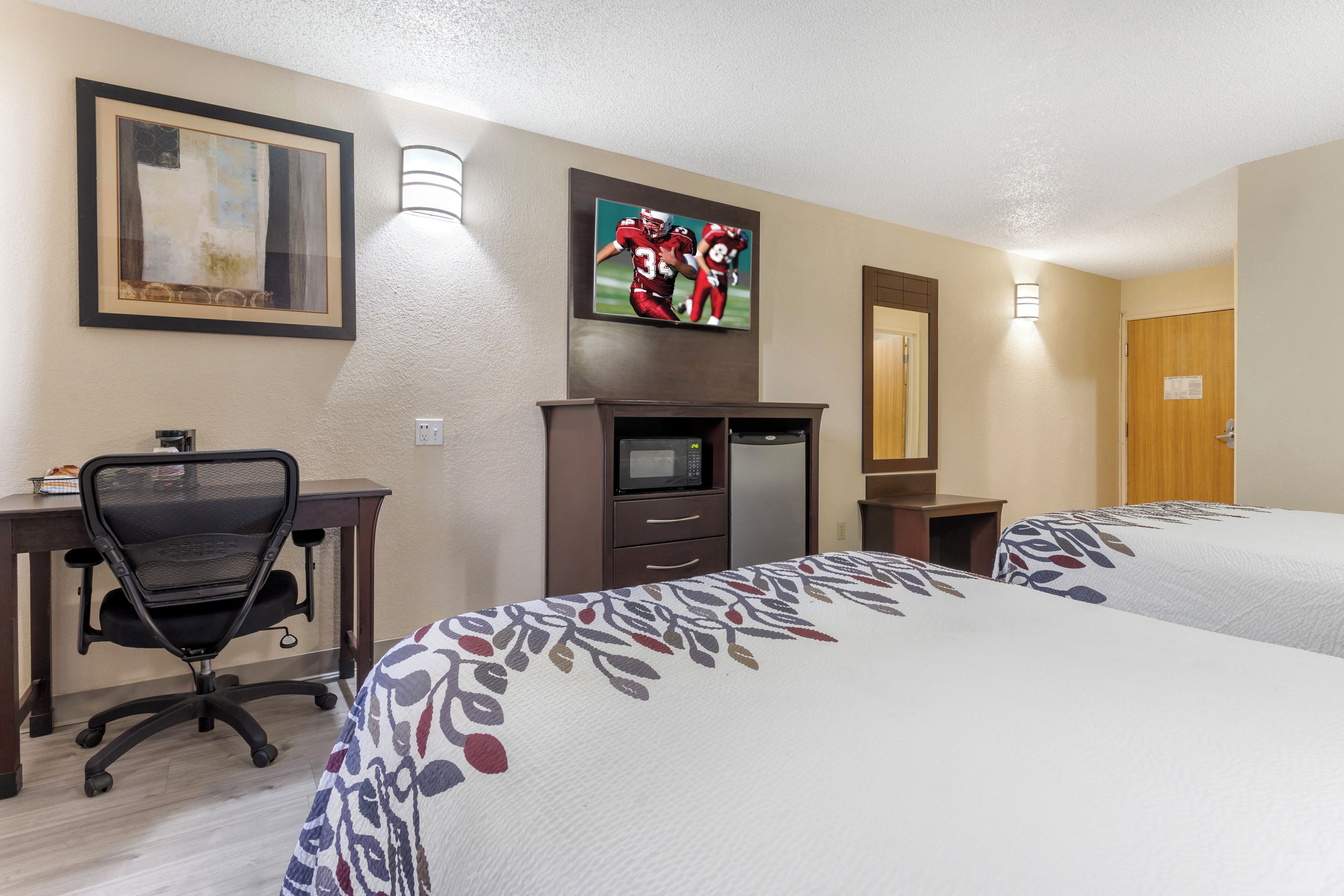 A hotel room with two beds, a desk with a chair, a television, and a microwave.