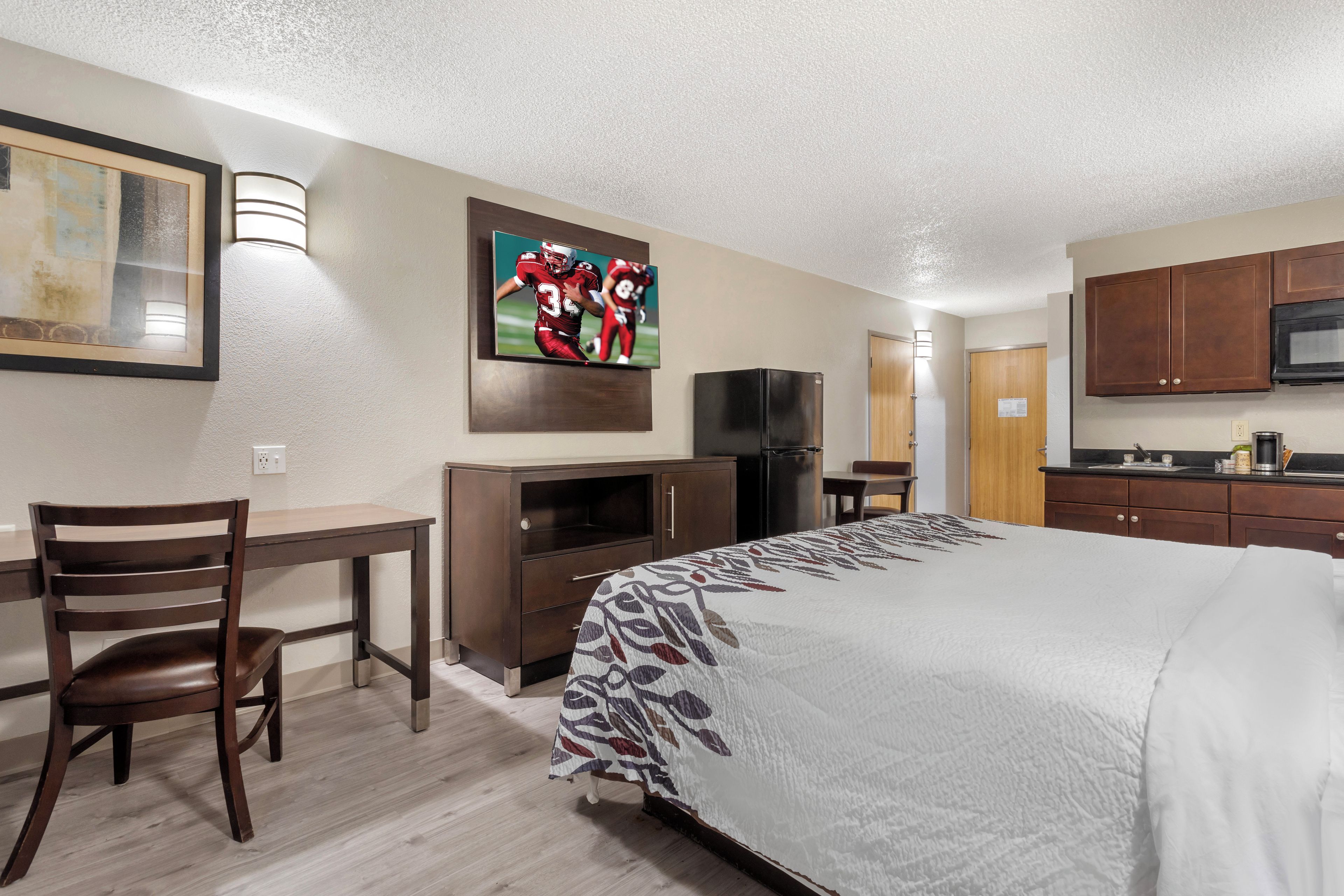 Una habitación de hotel con cama, escritorio, silla, televisor, refrigerador y armarios de madera.