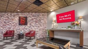 Un hall d’entrée de Red Roof Inn avec un sol à carreaux, deux fauteuils rouges, une table basse, une cheminée et un panneau indiquant que le Wi-Fi est disponible gratuitement dans toutes les chambres.